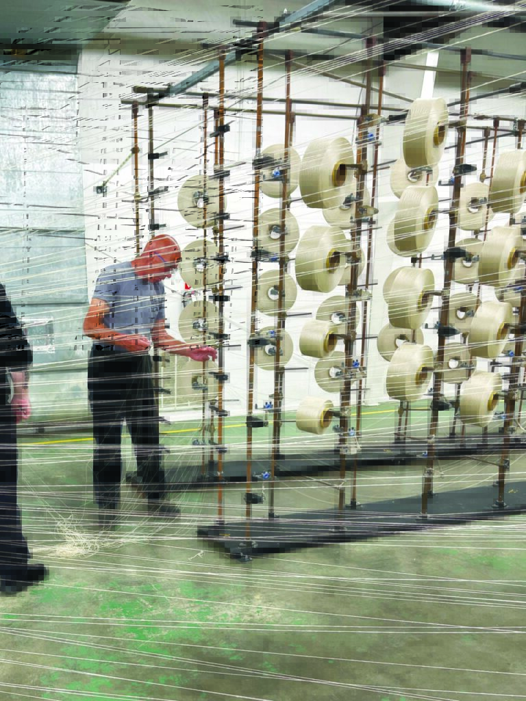 MMI Textiles plant engineer Roland Hossli inspects spools of fiber on a vertical rack, surrounded by fiber strands in a bright, industrial space.