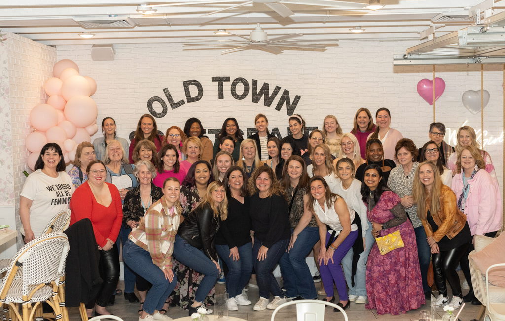 Group photo of diverse women smiling and posing together in a bright, welcoming venue with pink balloons and 'OLD TOWN' backdrop.