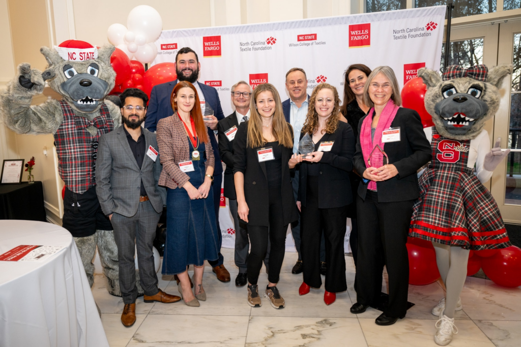 A group of individuals poses for a photo with a wolf mascot, surrounded by red and white balloons, celebrating an event.